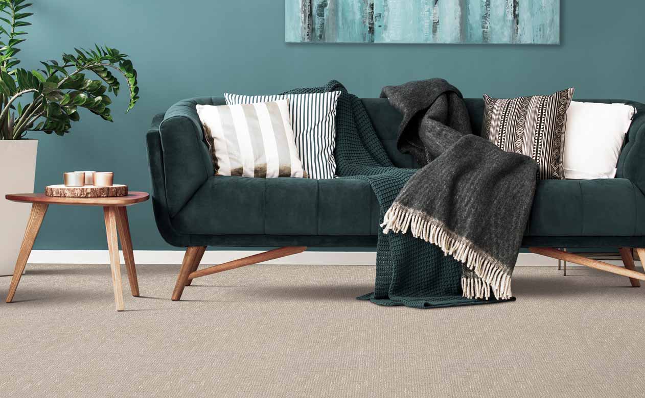 Beige textured carpet in modern living room with velvet green couch and blue accent wall